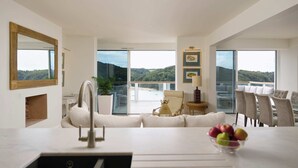 Een moderne woonkamer met een groot raam, een eethoek en een keuken met een spoelbak.