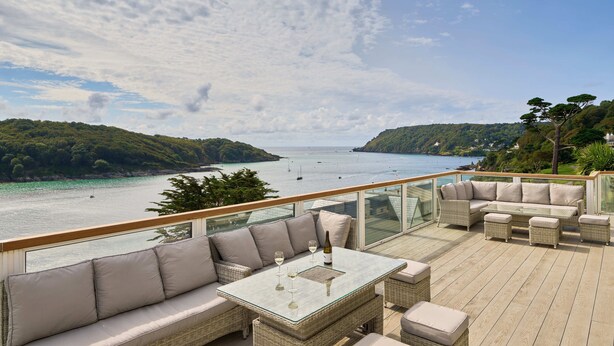 Een terras met buitenmeubilair, een glazen tafel en een prachtig uitzicht op zee en heuvels.