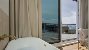 Een moderne badkamer met een vrijstaand bad, een douchecabine van glas en uitzicht op een balkon met tuinmeubilair.