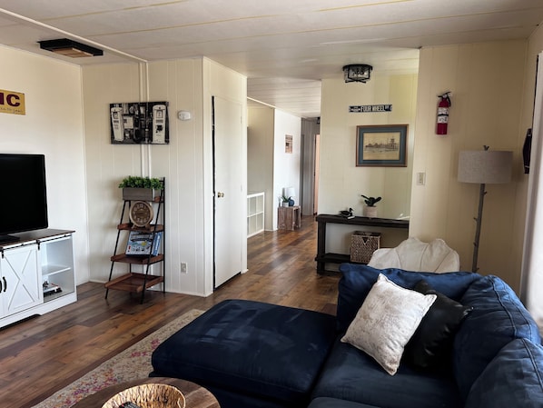 A living room with a dark blue sofa, a flat-screen TV on a cabinet, a bookshelf, and a hallway leading to another room. - Lakeview, boat parking, enclosed yard, pets welcome, peaceful & safe culdesac  (Lake Havasu City)