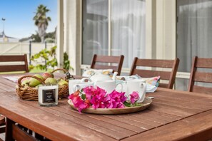 A wooden table with a white candle, teacups, and a plate of pink flowers.