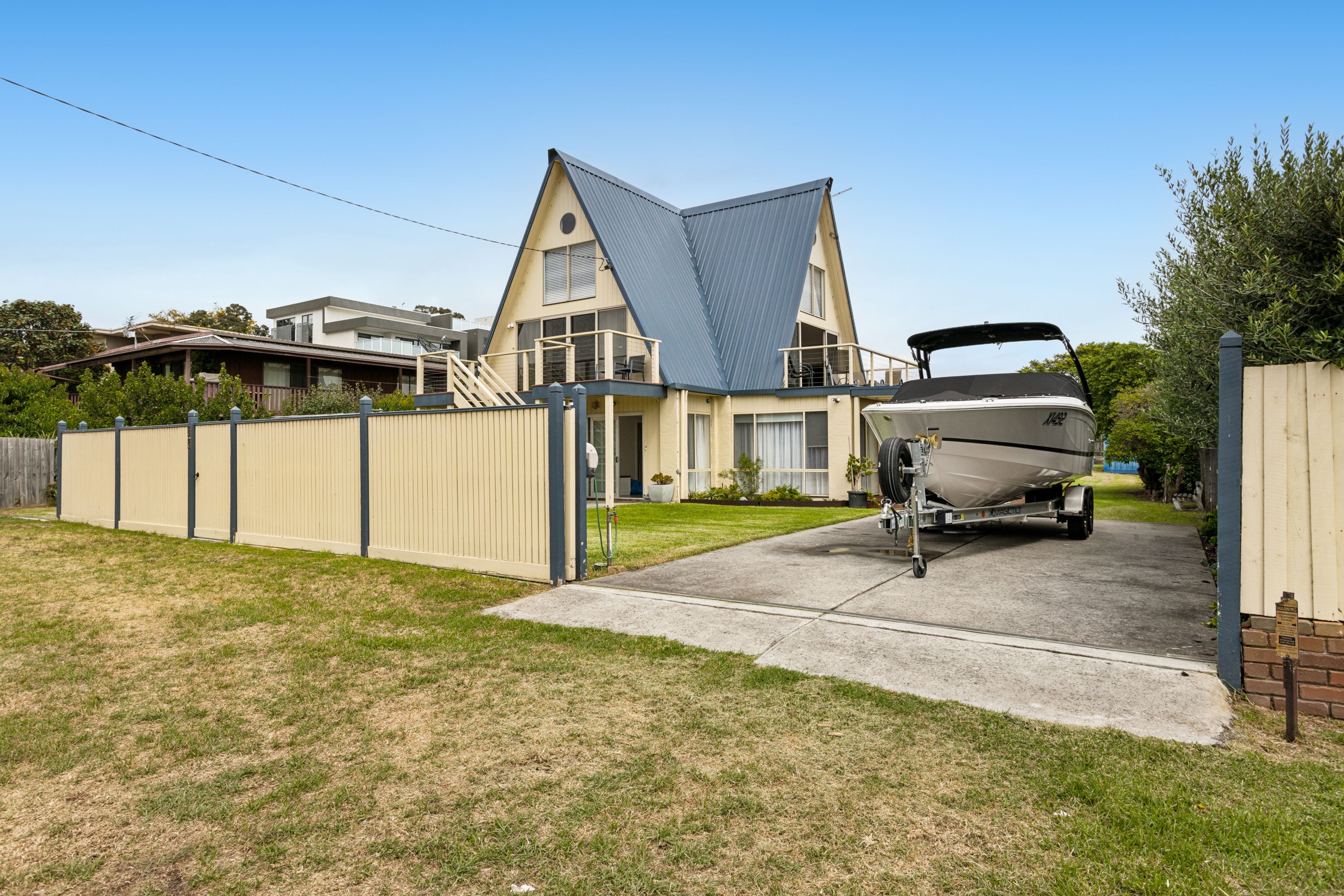 A residential property with a boat trailer in the driveway, a fenced yard, and a house with a distinctive gable roof.