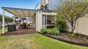 A covered outdoor area with a table and chairs, a barbecue grill, and a garden with various plants. - Rye Beach Chalet and Loft (Rye)