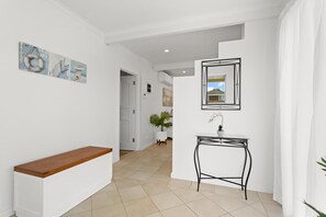 Un pasillo con un banco blanco, una pequeña mesa con una planta en maceta y un cuadro en la pared.
