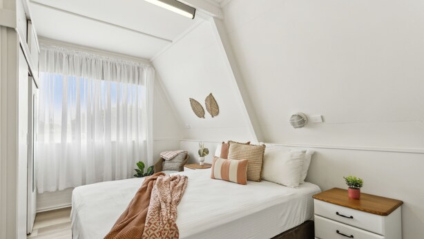 A bedroom with a bed, bedside tables, a window with curtains, and wall decorations. - Rye Beach Chalet and Loft (Rye)