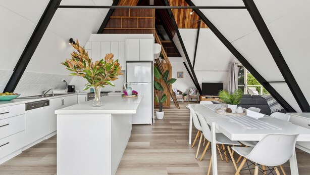Een moderne keuken met witte kasten, een centraal eiland en een eetgedeelte met witte stoelen.