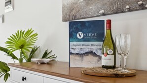 A wine bottle and glass on a wooden table with a framed poster in the background. - Rye Beach Chalet and Loft (Rye)