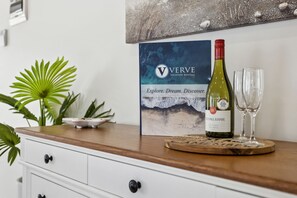 Una botella de vino y una copa sobre una mesa de madera con un cartel enmarcado al fondo.