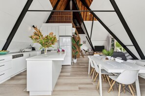 A modern kitchen with white cabinetry, a central island, and a dining area with white chairs. - Rye Beach Chalet and Loft (Rye)