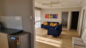Una sala de estar moderna con un sofá azul, una silla blanca y una pequeña kitchenette.