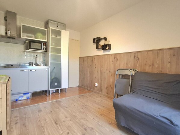 Cocina compacta con microondas, armarios y pileta. Se observan paneles de madera en la pared y un sofá gris.