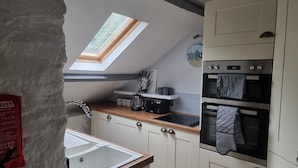 A compact kitchen with a skylight, a sink, a stove, and a clock on the wall. - Stunning 2-bed House in Saint Columb (Newquay)