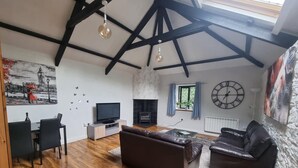 A spacious living room with a high ceiling, wooden flooring, a fireplace, a television, and a large clock on the wall. - Stunning 2-bed House in Saint Columb (Newquay)