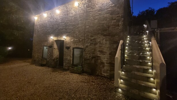 A stone building with a staircase leading to an entrance, illuminated by string lights. - Stunning 2-bed House in Saint Columb (Newquay)