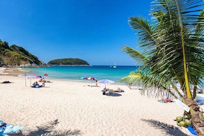 A beach with clear blue water, umbrellas, and a palm tree.