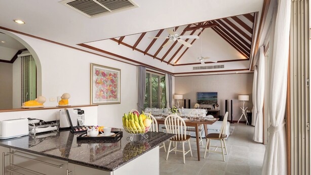 A modern kitchen with a central island, dining area with chairs, and a large window. - Katamanda 3 Bed Tropical Villa B3 Near Kata Beach (Karon)