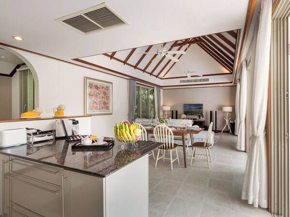 A modern kitchen with a central island, dining area with chairs, and a large window. - Katamanda 3 Bed Tropical Villa B3 Near Kata Beach (Karon)