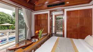 A spacious bedroom with a large bed, wooden wardrobe, and a view of a swimming pool. - Katamanda 3 Bed Tropical Villa B3 Near Kata Beach (Karon)
