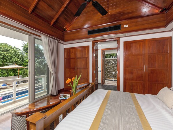 A spacious bedroom with a large bed, wooden wardrobe, and a view of a swimming pool. - Katamanda 3 Bed Tropical Villa B3 Near Kata Beach (Karon)