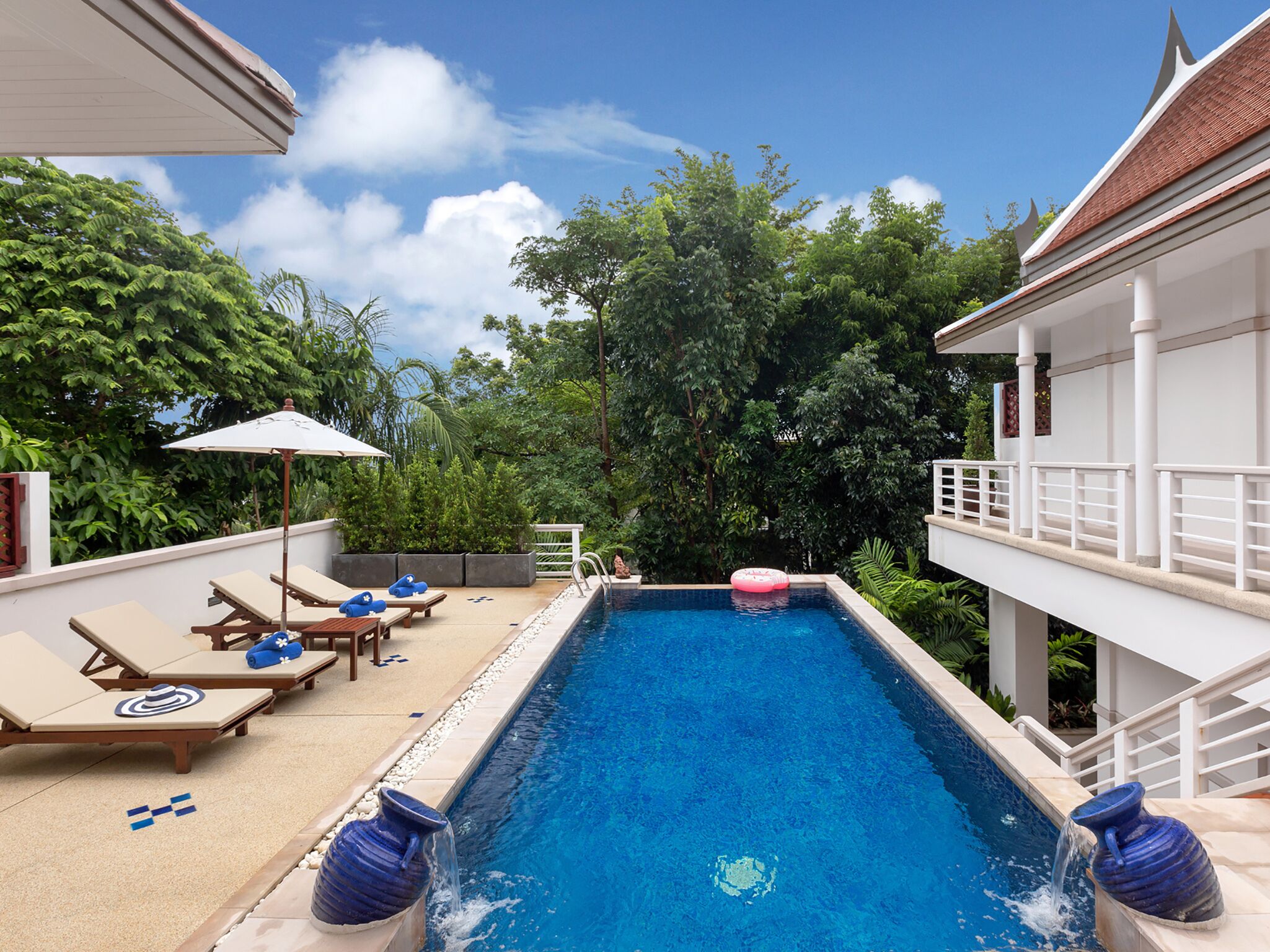 Une piscine entourée d’une végétation luxuriante, avec des chaises longues et des parasols.