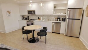 A modern kitchen with white cabinetry, a stainless steel refrigerator, a microwave, a stove, and a dishwasher. There is a round table with two chairs.