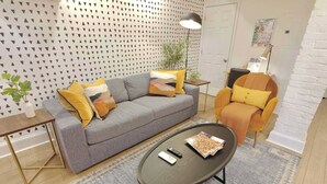 A modern living room with a grey sofa, a round coffee table, a yellow armchair, and a patterned wall.