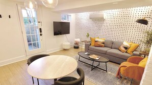 A modern living room with a grey sofa, a round wooden table, and a TV mounted on the wall.