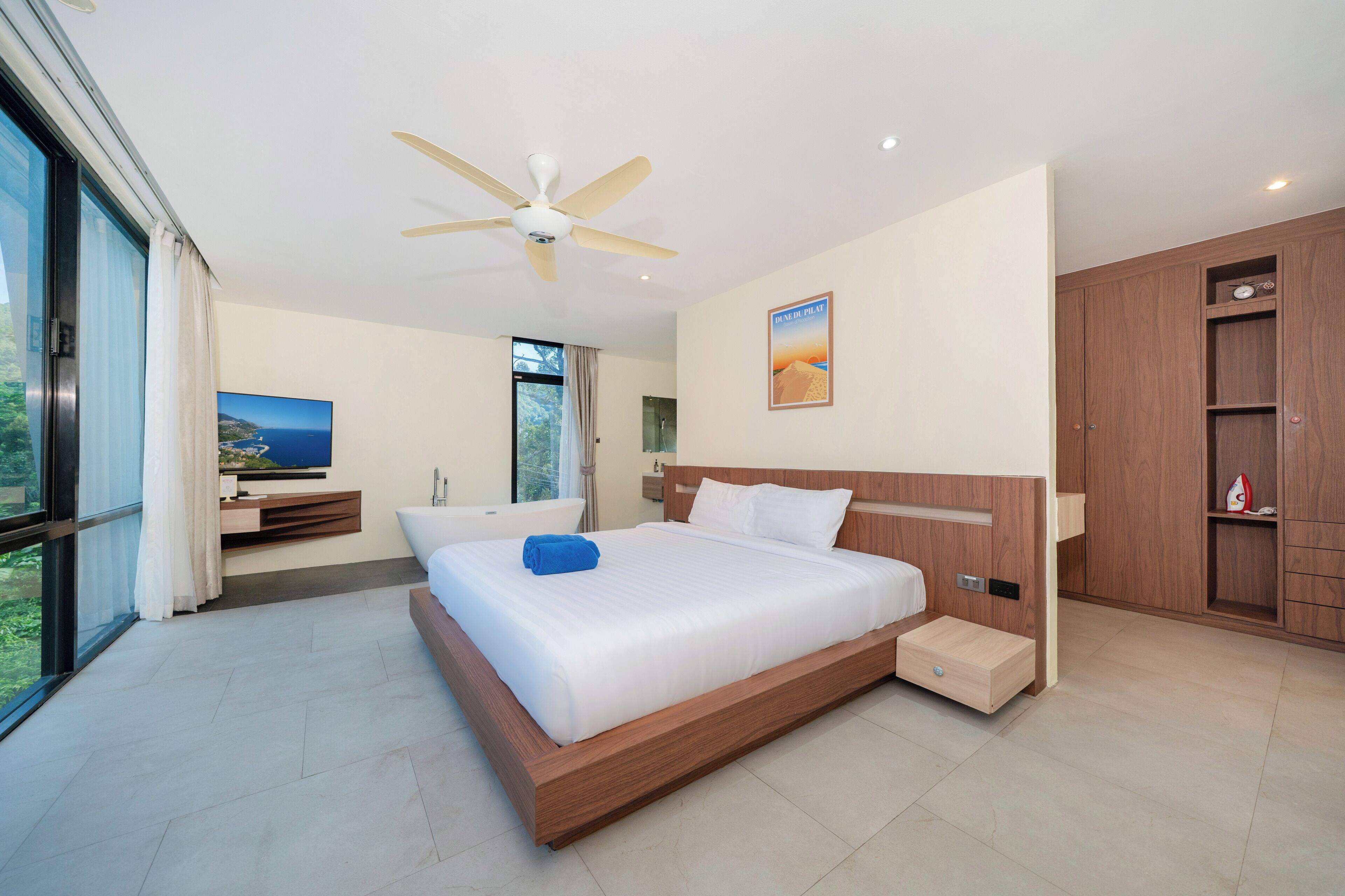A modern hotel room with a large bed, a ceiling fan, a TV, and a view of the outdoors.