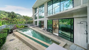 Ett modernt hus i två våningar med en swimmingpool, en uteplats och utsikt över den omgivande naturen.