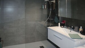 Ein modernes Badezimmer mit einer Glasdusche, einem weißen Waschbecken und einem Spiegel darüber.
