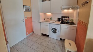 Una cocina compacta con armarios blancos, lavadora, lavaplatos y un taburete pequeño.