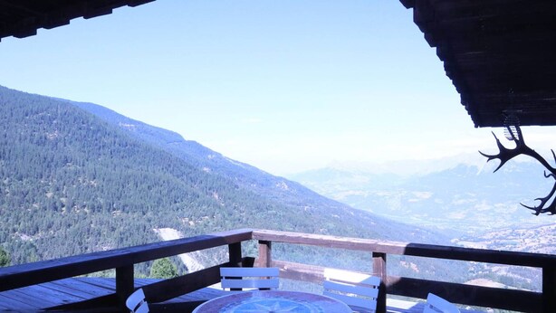 A wooden deck with a round table and white chairs, overlooking a mountainous landscape.