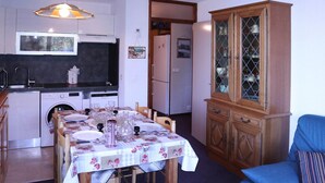 A compact kitchen with modern appliances, a dining table set for four, and a cabinet with glass doors.