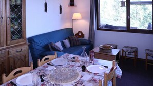 A dining area with a table set for four, a blue sofa, a cabinet with glass doors, and a window with a view of trees.