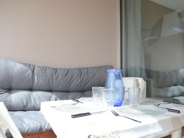 Ein Esstisch ist gedeckt mit Tellern, Besteck und Gläsern, vor einer grauen Couch und einem Fenster platziert.