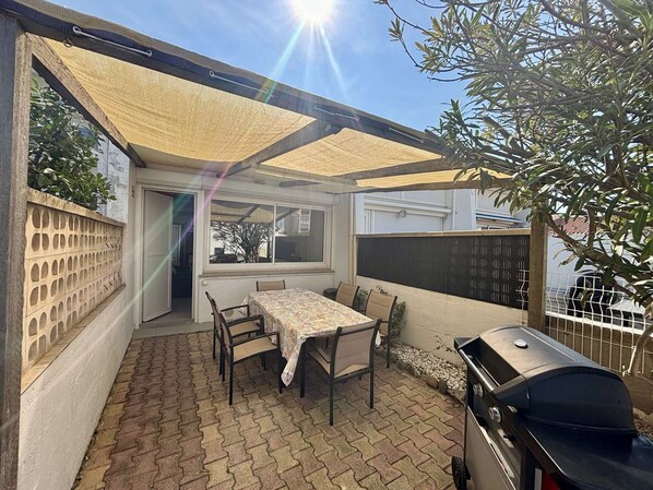 A patio with a table and chairs, a grill, and a covered area with a view of the street.