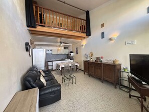 A compact living space with a kitchenette, a dining area, a black leather sofa, a TV, and a balcony.