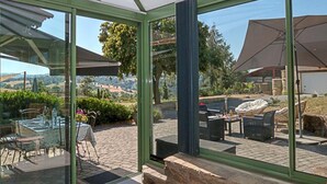 Un porche con paredes de cristal, mobiliario exterior, una mesa y vistas al campo.
