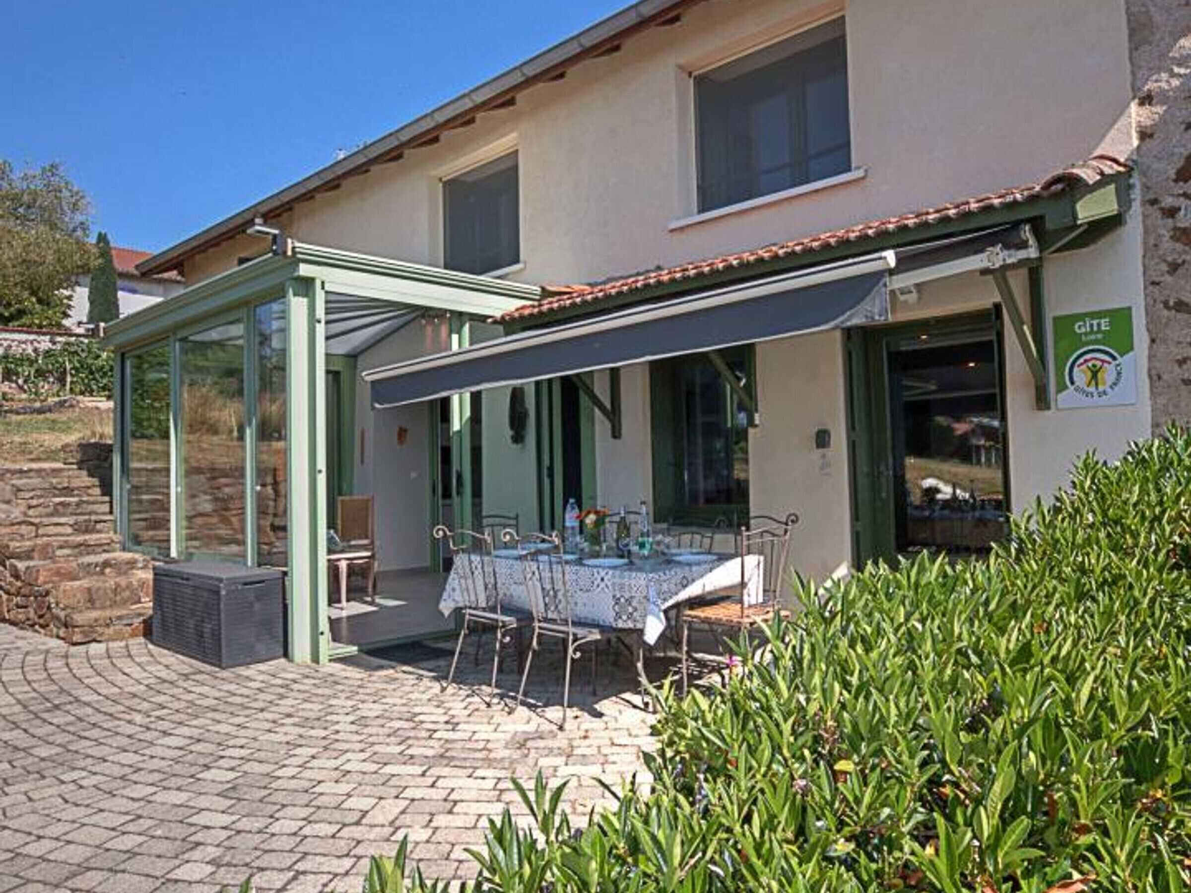 A house with a covered patio, a table with chairs, and a sign indicating it's a Gîte.