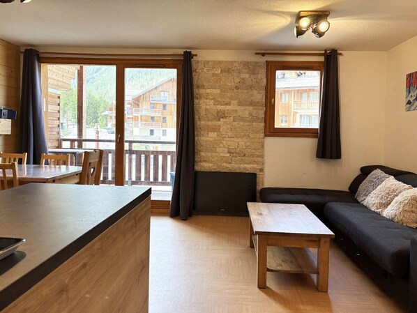Una stanza con un tavolo di legno, un divano, un muro in pietra e un balcone che si affaccia su edifici.