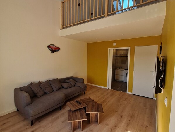 A living room with a gray sofa, two wooden coffee tables, a wooden railing, and a door leading to a laundry area. - Renovated home near Nancy and Metz, pet-friendly (Lironville)