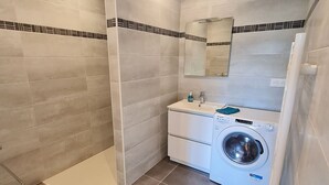 Ein Badezimmer mit grauen Fliesen, einer Waschmaschine, einem Waschbecken und einem Spiegel.
