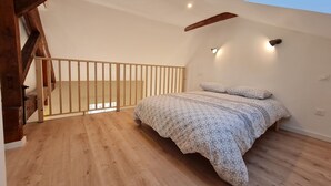 Ein Schlafzimmer mit schrägverdeckter Decke, Holzboden und einem Bett mit gemusterten Bettbezügen.