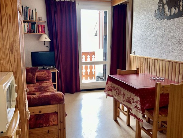 Um quarto aconchegante com um sofá de madeira, uma mesa de jantar com cadeiras, uma televisão e uma estante de livros.