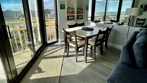 Uma sala de estar moderna com área de jantar, janelas amplas e vista para o mar.