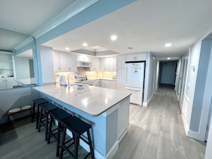 A modern kitchen with a large island, white cabinetry, and a stainless steel refrigerator. - Oceanfront 3/3-This Is the One You Have Been Waiting For! All New+ Beach Locker! (Myrtle Beach)