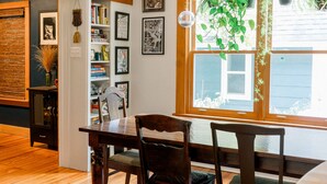 A dining area with wooden flooring, a dining table with chairs, a hanging plant, and a bookshelf with books and decorative items. - Blue Dream: Romantic Getaway with hot tub, sauna, fireplace. Near downtown. (Yellow Springs)