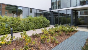 Un edificio moderno con amplios ventanales y un jardín ajardinado con diversas plantas y un camino.