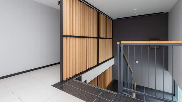 Un interior moderno con una escalera, un panel de madera y una barandilla negra.