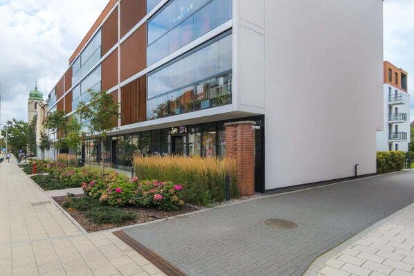 A modern building with large windows, a brick base, and a paved walkway with flower beds. - Stylish Apartment with a Balcony | Gdansk Wrzeszcz (Gdansk)